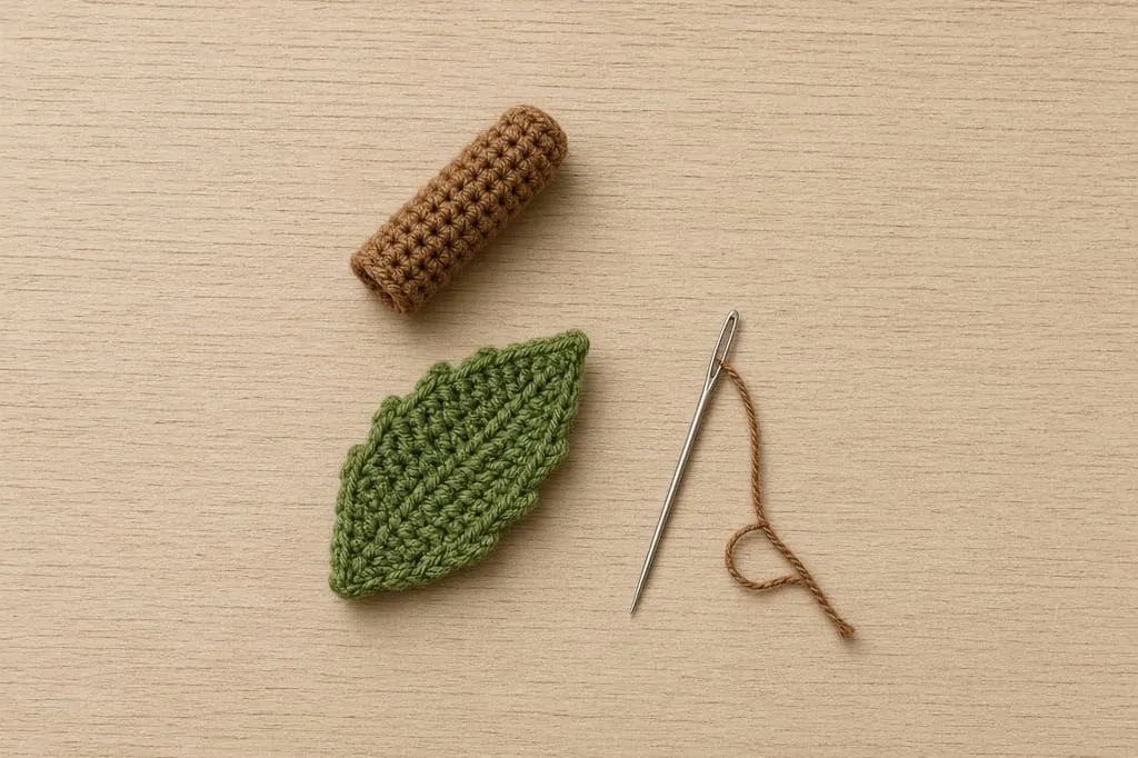 A small crocheted brown tube and a green leaf shape lying beside a tapestry needle