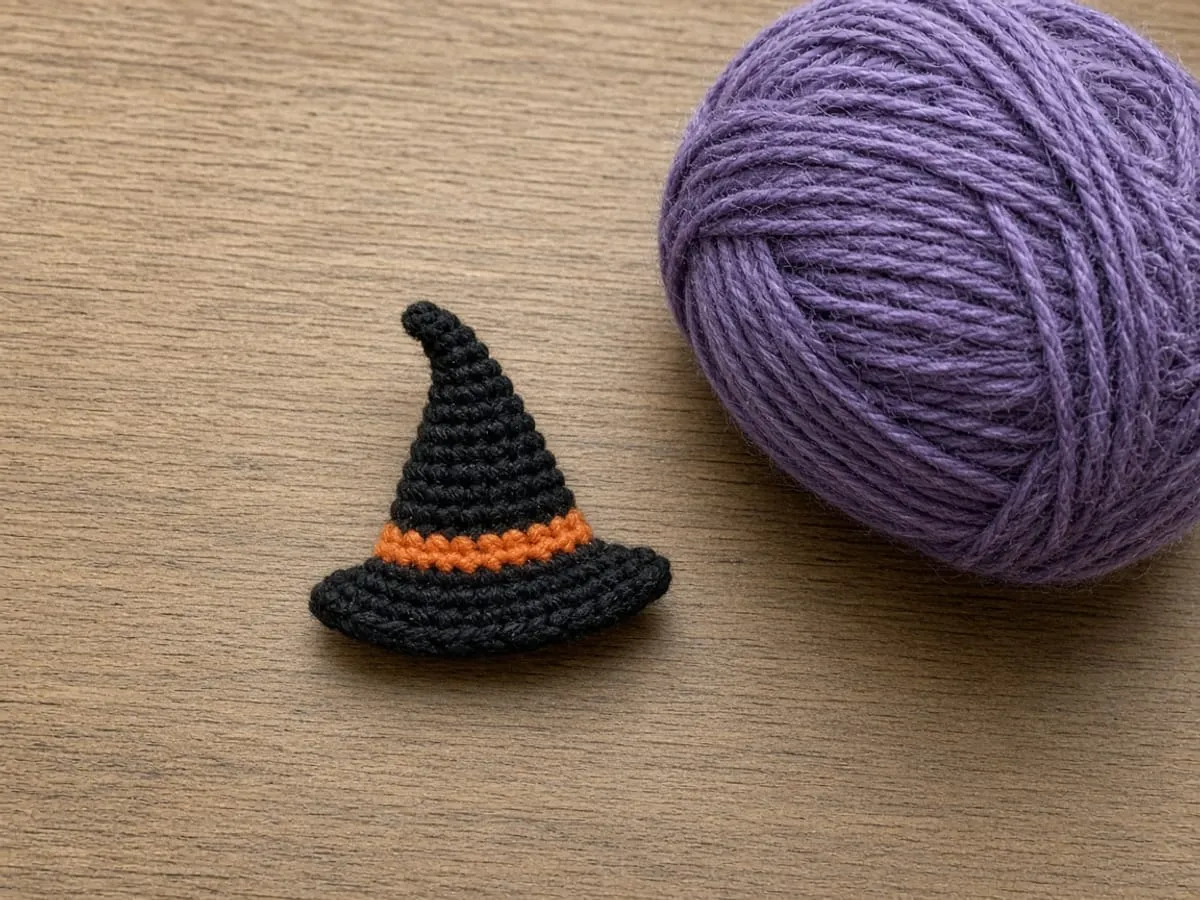 The small black hat with an orange band, beside a ball of purple yarn